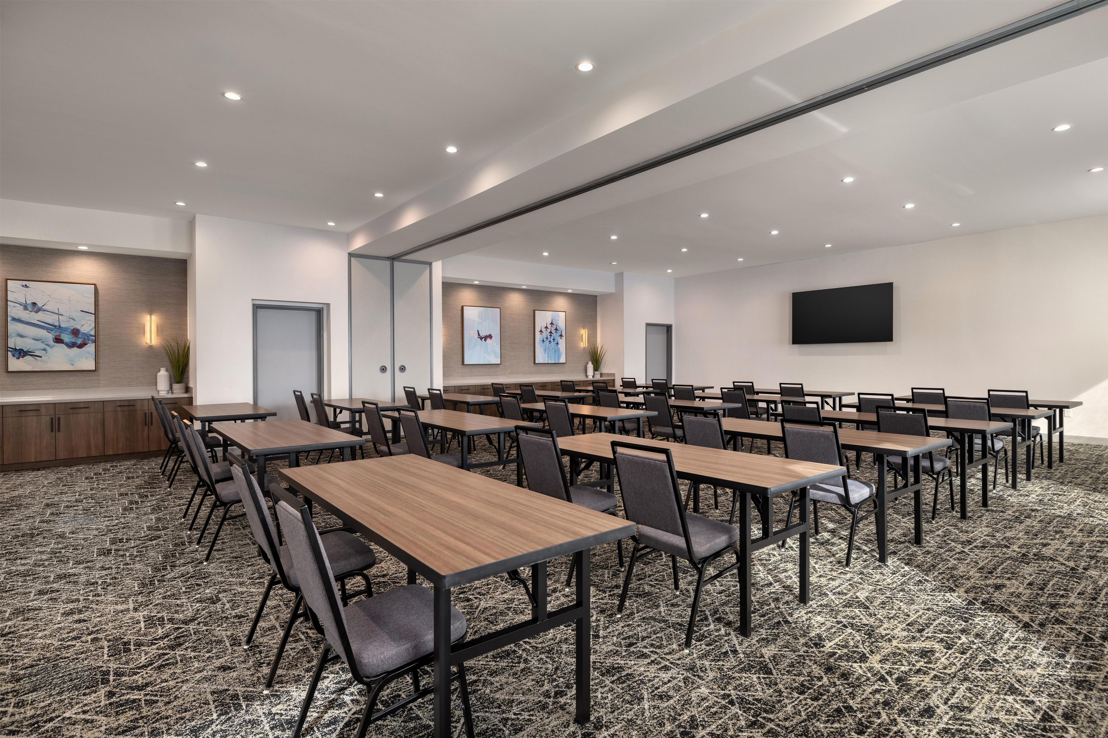 A conference room with multiple tables and chairs, a flat-screen TV mounted on the wall, and artwork on the walls.