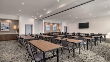 A conference room with multiple tables and chairs, a flat-screen TV mounted on the wall, and artwork on the walls.