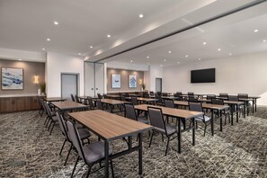 Une salle de conférence équipée de plusieurs tables et chaises, d’un téléviseur à écran plat fixé au mur et d’œuvres d’art accrochées aux murs.