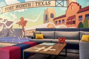Une pièce décorée d’une fresque représentant Fort Worth, au Texas, avec un canapé aux coussins jaunes, une table basse sur laquelle on peut jouer aux dominos, et des sièges aux couleurs vives.