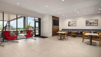 Un interior moderno con una zona de estar que incluye sillas rojas y una silla colgante, un comedor con sillas amarillas, y un ventanal con vistas.