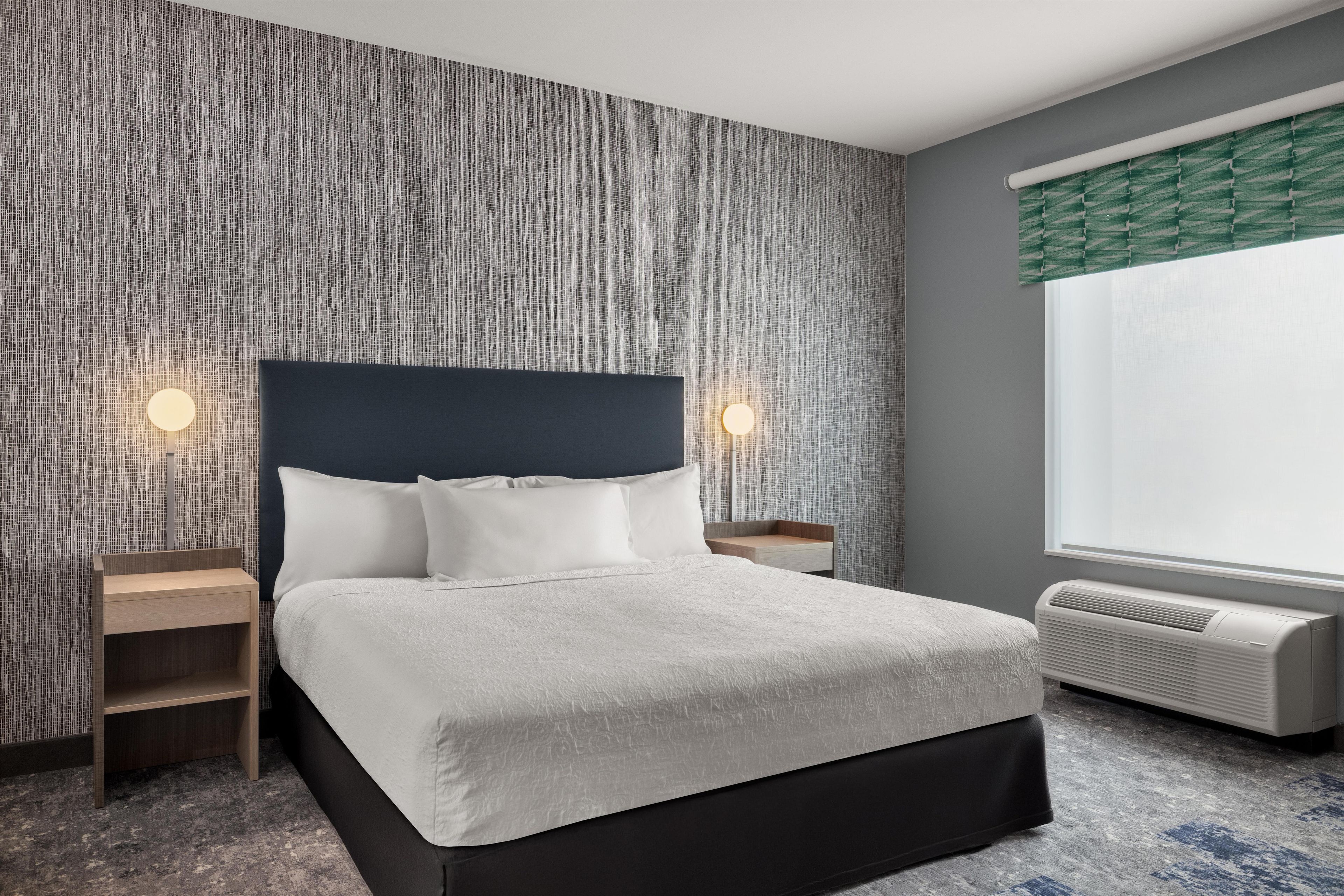 A hotel room with a bed, bedside tables, a wall-mounted heater, and a window with a view.