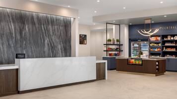 A modern hotel reception area with a marble reception desk, a wall-mounted artwork, and a cold beverage bar with snacks.