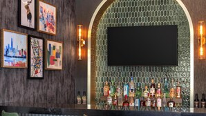 Eine Bar mit modernem Design, inklusive eines großen Bildschirms, einer Auswahl an Spirituosenflaschen und grünen gepolsterten Barhocker.