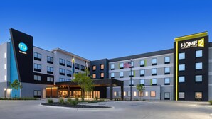 Ein modernes Hotel mit einem gut sichtbaren Schild 'tru by Hilton', mehreren Etagen und einem einladenden Eingangsbereich mit Vordach und einer Flaggenpräsentation.