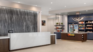A modern hotel reception area with a marble reception desk, a cold beverage refrigerator, and a minibar. - Tru By Hilton Fort Worth Lake Worth (Fort Worth)