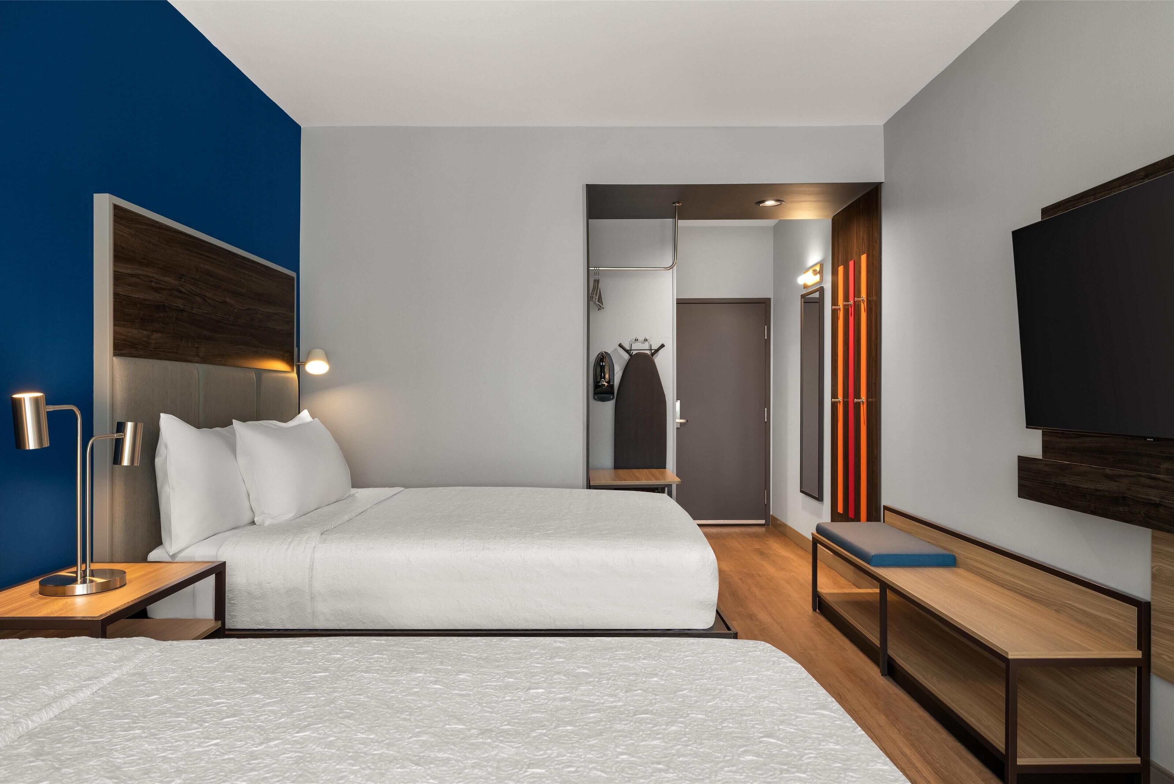 A modern hotel room with a large bed, bedside tables, a bench, a TV, and a wardrobe.