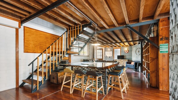 A spacious kitchen with a large island, wooden bar stools, and a staircase leading to an upper level. - The Workshops - Clyde Holiday Home (Clyde)