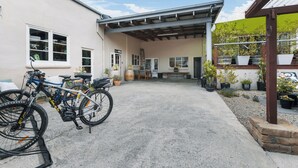 A covered patio area with a concrete floor, bicycles, and potted plants. - The Workshops - Clyde Holiday Home (Clyde)
