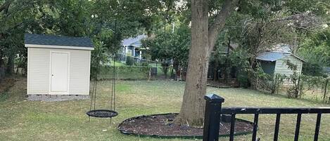 A wooden deck with a metal railing, a swing set, and a small shed in a backyard with a tree.
