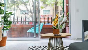 Een moderne woonkamer met een grote glazen deur die leidt naar een terras, een ronde houten tafel met een potplant en een zwart-wit tapijt.