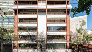 Een meerlaags gebouw met balkons, een garage-ingang en een boom ervoor.