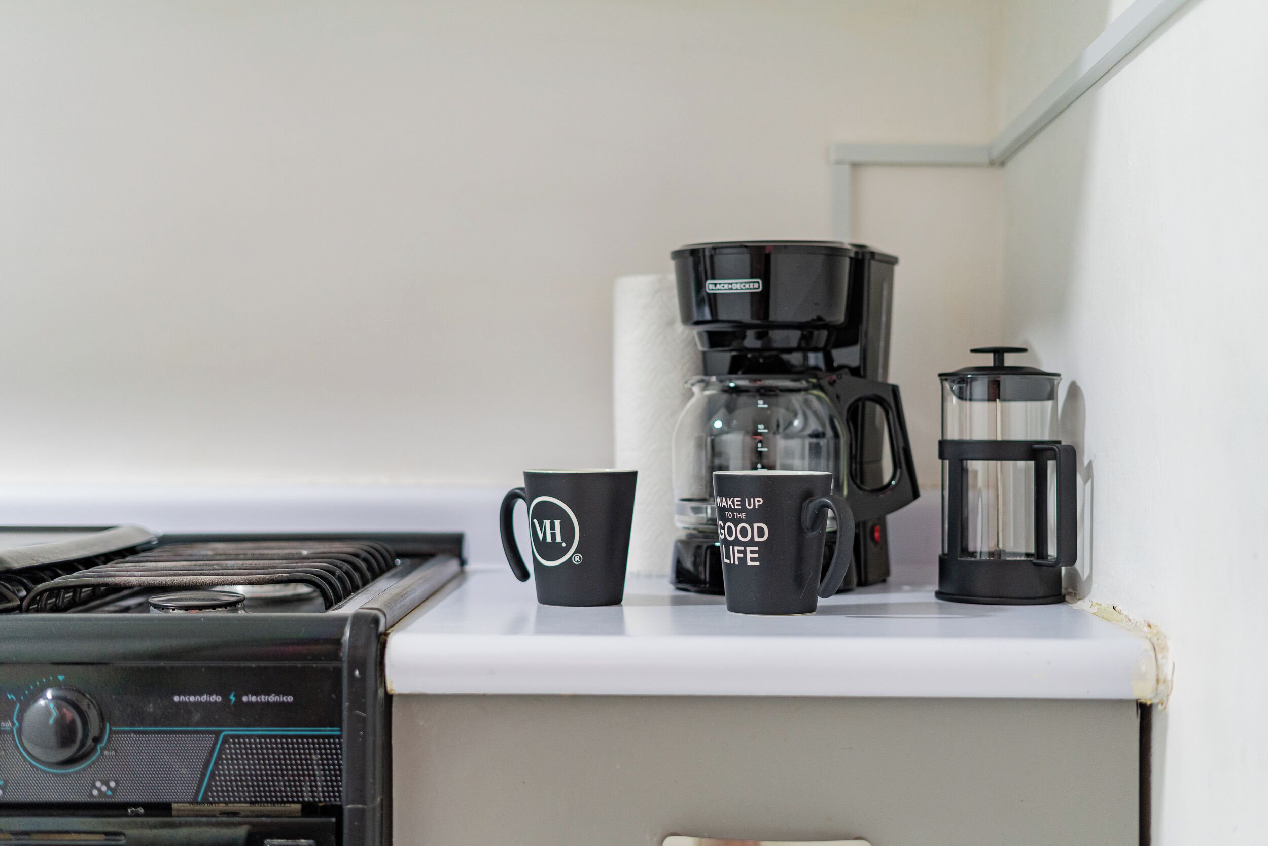 Et tekøkken med kaffemaskine, presskanne og to sorte kopper på bordet.