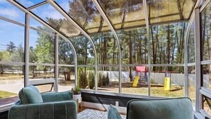A conservatory with a glass ceiling, two green cushioned chairs, and a view of a playground. - Strawberry Pines Retreat (Strawberry)