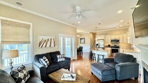 A spacious living room with a sofa, ottoman, and coffee table, a dining area with chairs, and a kitchen with modern appliances.