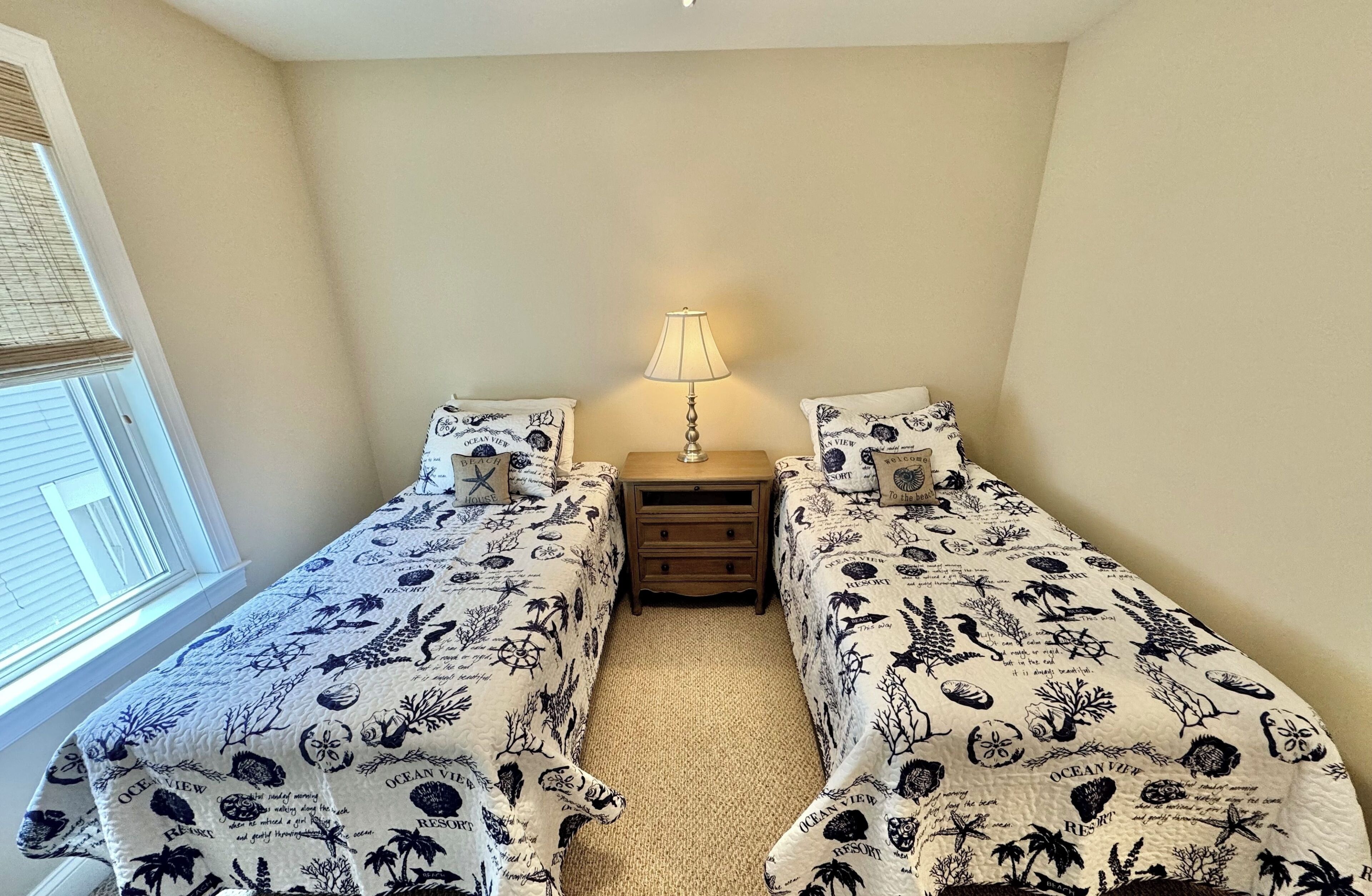 A bedroom with two beds, a nightstand, a lamp, and a window with blinds.