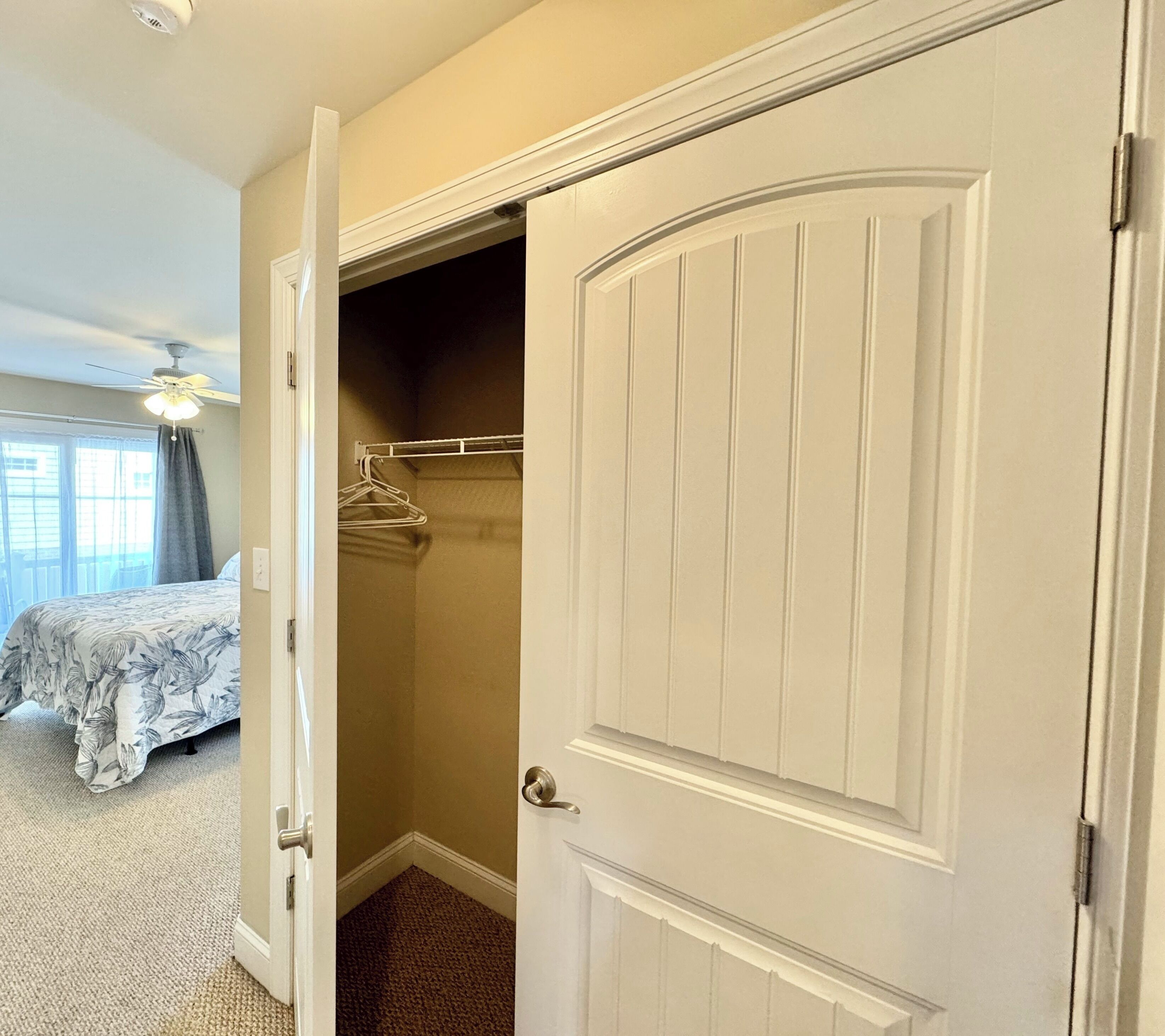 A bedroom with a bed, a closet with a hanging rod, and a ceiling fan.