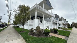 A two-story residential building with a covered front porch, a small front yard with a tree and shrubs, and a visible street sign indicating a speed limit of 15 mph.