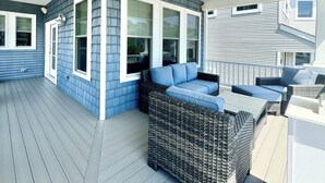 A covered outdoor deck with a wicker sofa and a table, a covered porch with a window, and a railing.