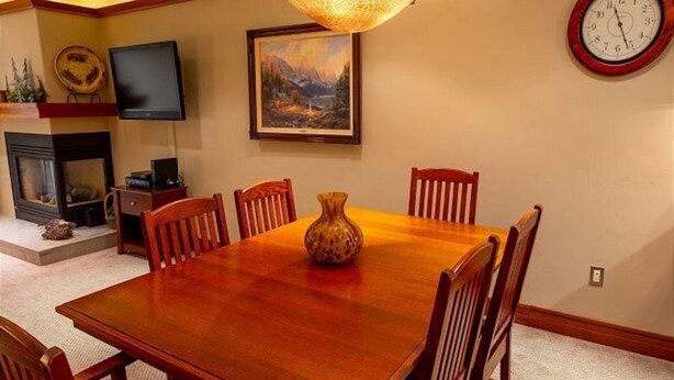 A dining room with a wooden table, six chairs, a vase, a painting, a clock, and a fireplace. - 1 Bedroom Condo at the Base of Aspen Mountain, Heart of Downtown (Aspen)