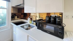 Eine kompakte Küche mit weißen Schränken, einer Edelstahl-Spüle, einer schwarzen Mikrowelle und einer Kaffeemaschine.