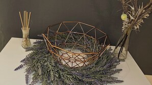 Ein Tisch mit einem geometrischen Drahtkorb, einer Glasvase mit getrockneten Blumen und einer Schale mit Räucherstäbchen.