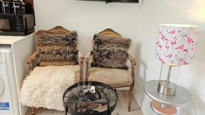Ein Wohnzimmer mit zwei Sesseln, einem Glastisch, einer Lampe und einem Fernseher an der Wand.
