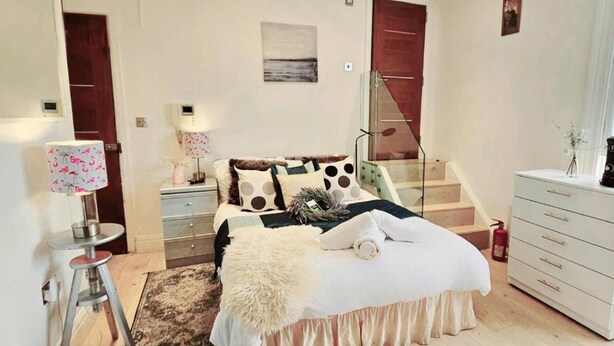 Ein Schlafzimmer mit Bett, Nachttisch, Lampe, Kommode und einer Treppe.