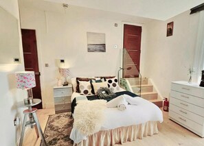 A bedroom with a bed, a nightstand, a lamp, a dresser, and a staircase. - Chic Studio in Central London (London)