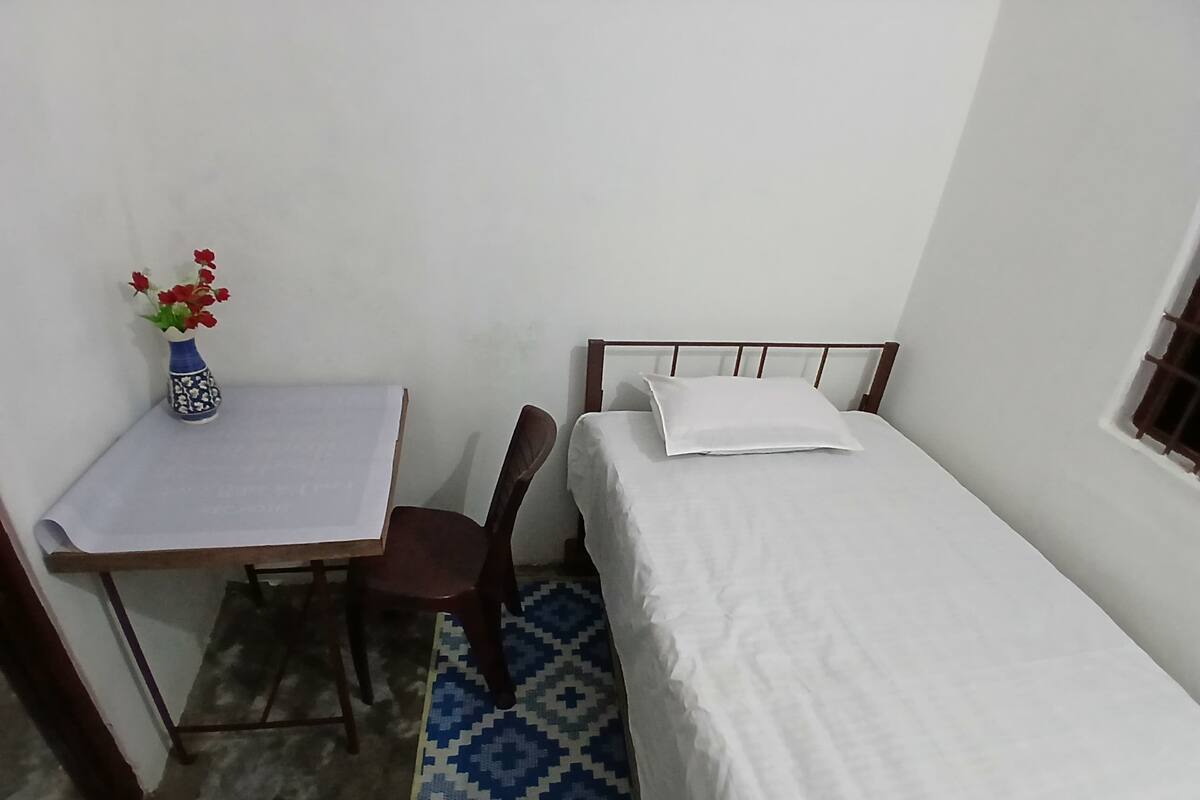 A small, simple room with a bed, a desk, and a chair.