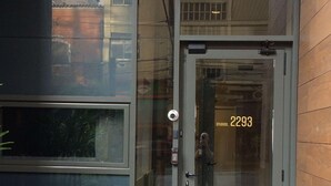 Une entrée moderne, avec une porte en verre portant l’inscription « 2293 » et une caméra de surveillance.