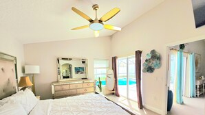 A hotel room with a bed, a dresser, a ceiling fan, a large mirror, and a view of a pool.