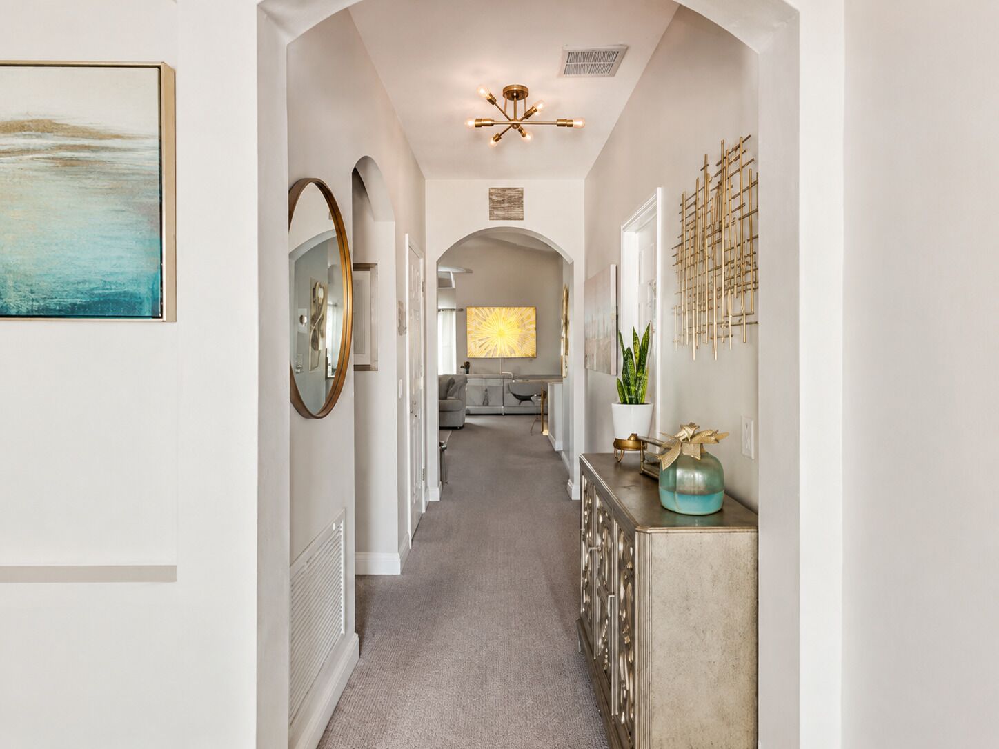 A hallway with a mirror, a ceiling light fixture, and a plant on a console table.