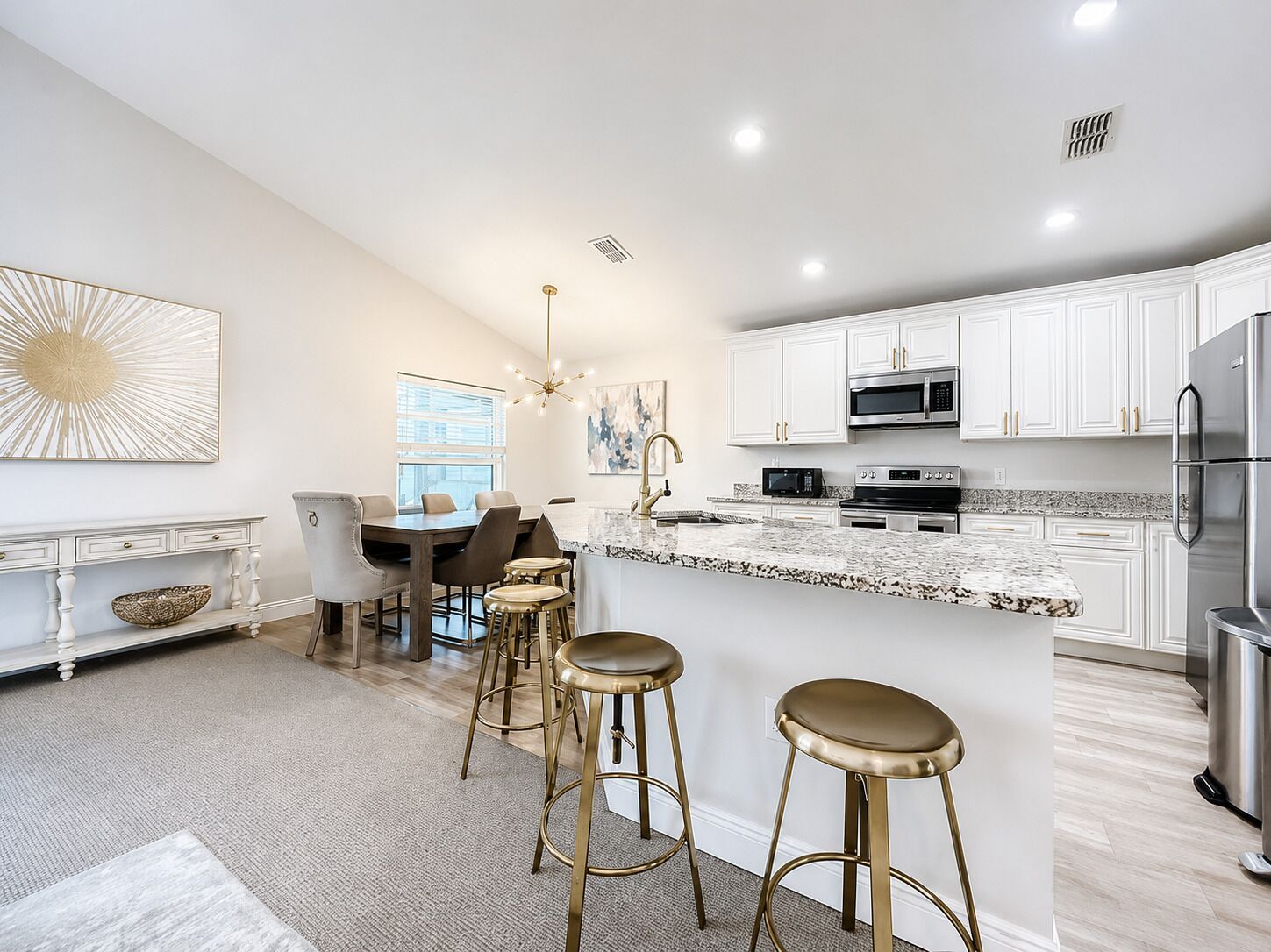 A modern kitchen with white cabinetry, stainless steel appliances, and a marble island with stools.