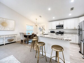 A modern kitchen with white cabinetry, stainless steel appliances, and a marble island with stools.