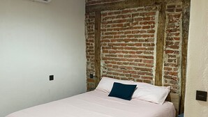 A bedroom with a brick wall, a bed with a pink bedspread, and a hanging light fixture. - 7 beds, 3bedR, Centro, SOL, Gran Via, metro Noviciado, Callao (Madrid)