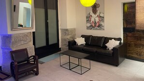 A living room with a black leather sofa, a small black coffee table, a wooden chair, a mirror, and colorful hanging lights. - 7 beds, 3bedR, Centro, SOL, Gran Via, metro Noviciado, Callao (Madrid)