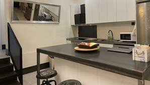 A modern kitchen with white cabinets, a stainless steel refrigerator, a microwave, and a small island with stools. - 7 beds, 3bedR, Centro, SOL, Gran Via, metro Noviciado, Callao (Madrid)