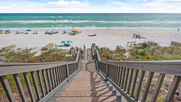 Eine Holztreppe führt zu einem Strand mit Sonnenschirmen und Liegestühlen.