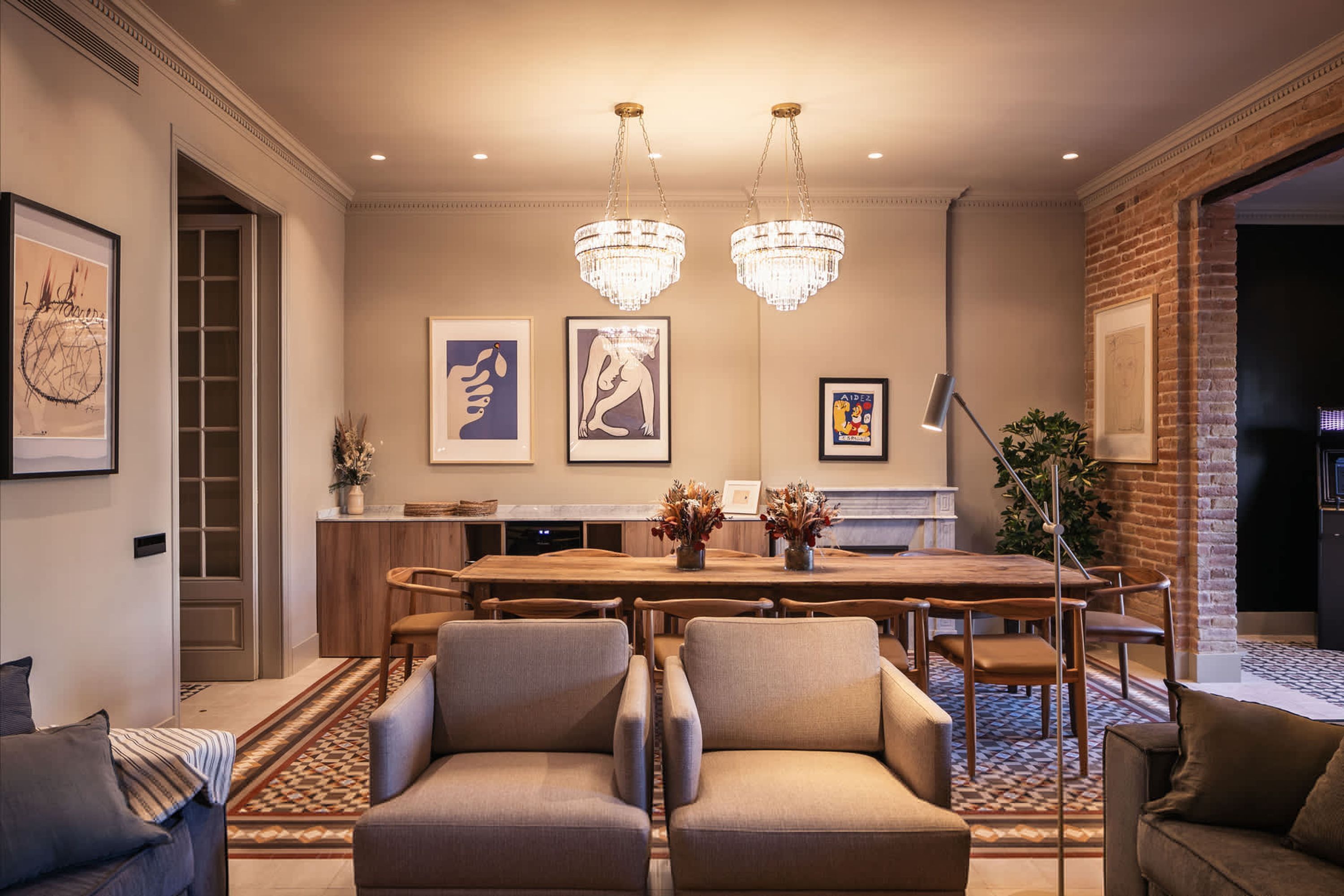 A modern dining area with a wooden table, two upholstered chairs, and a chandelier.