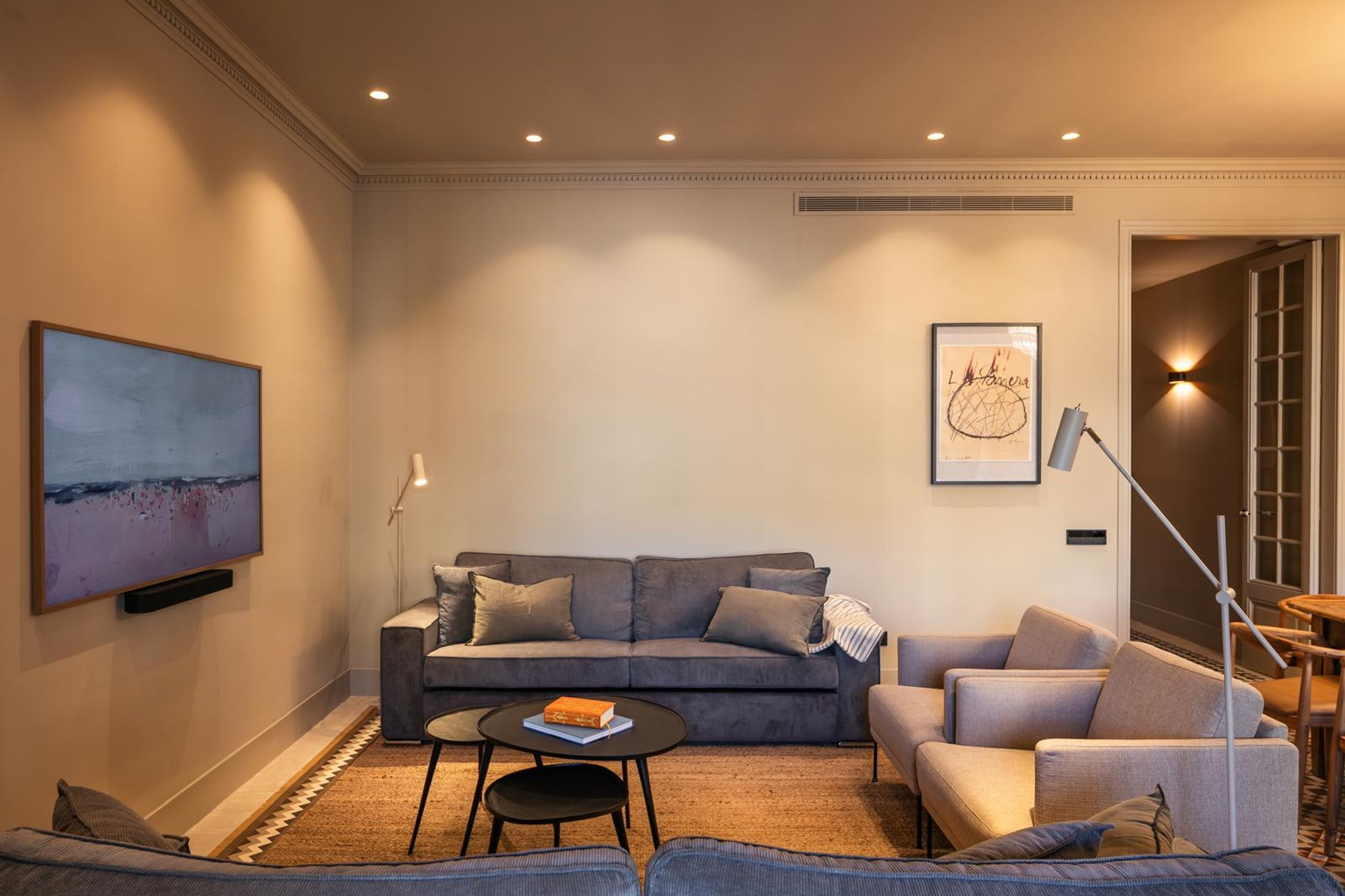 A modern living room with a grey sofa, a coffee table, and a flat-screen TV mounted on the wall.