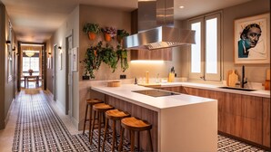 A modern kitchen with a central island, bar stools, a stainless steel range hood, and a backsplash with plants. - Lovely 6 BR Flat in L Eixample (Barcelona)
