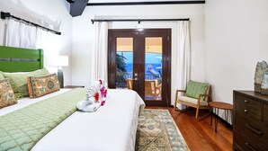Une chambre d’hôtel avec un lit, une chaise, une commode et une vue sur l’océan par la porte.