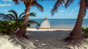 Une plage avec une jetée en bois menant à une structure surmontée d’un toit de chaume.