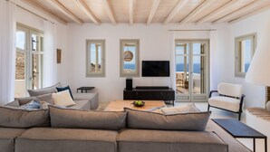 Ein modernes Wohnzimmer mit einer großen Couch, einem Fernseher und Meerblick durch große Fenster.