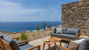 Eine Terrasse mit Holzmöbeln und einer Steinmauer mit Blick auf die Küste.