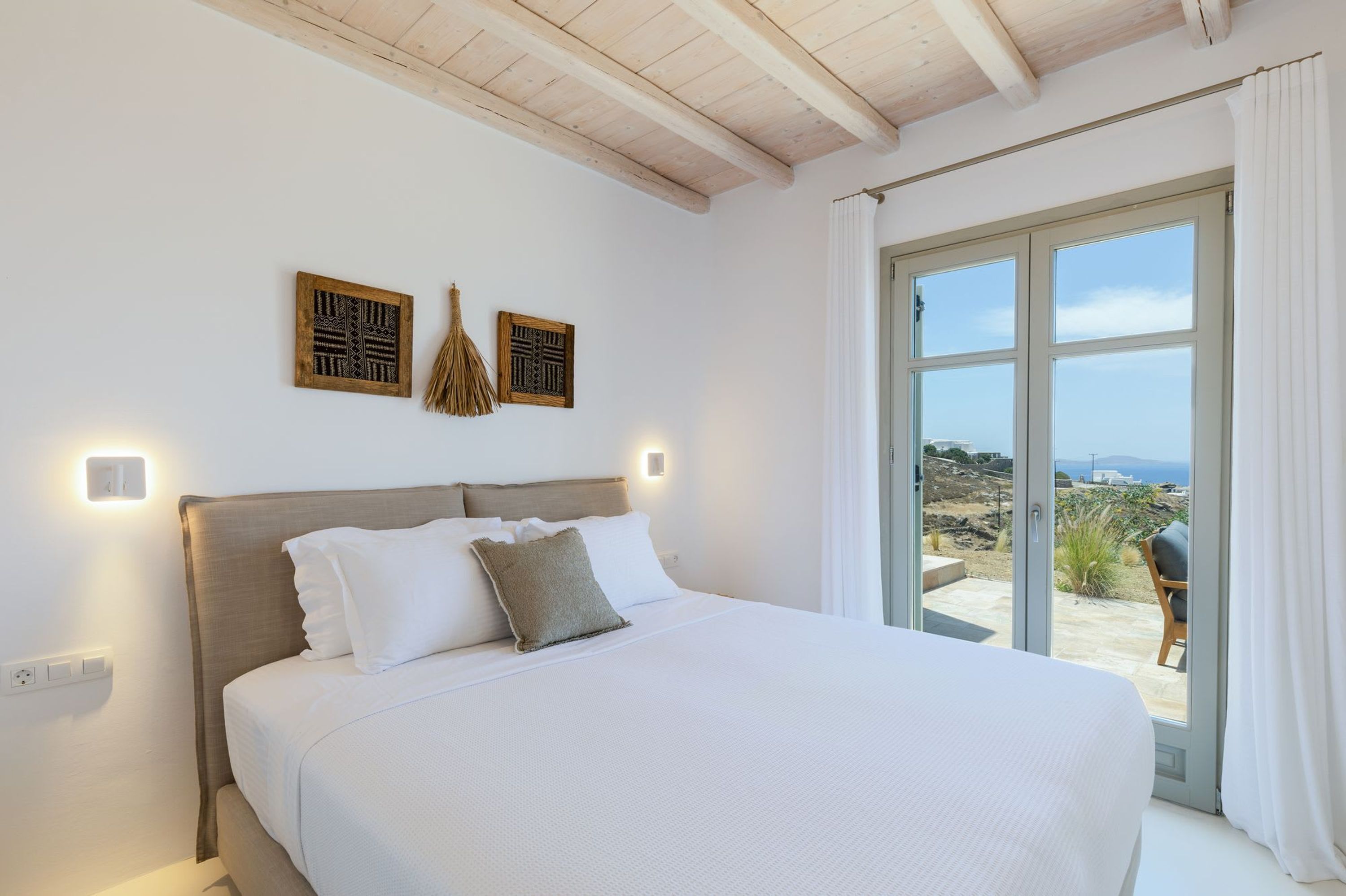 A bedroom with a large bed, a wooden ceiling, and a view of the outdoors through a sliding glass door.