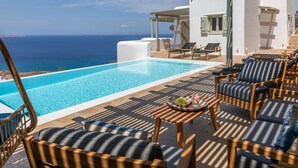 Ein Poolbereich mit Liegestühlen, einem Tisch mit Obstschale und Blick auf das Meer.