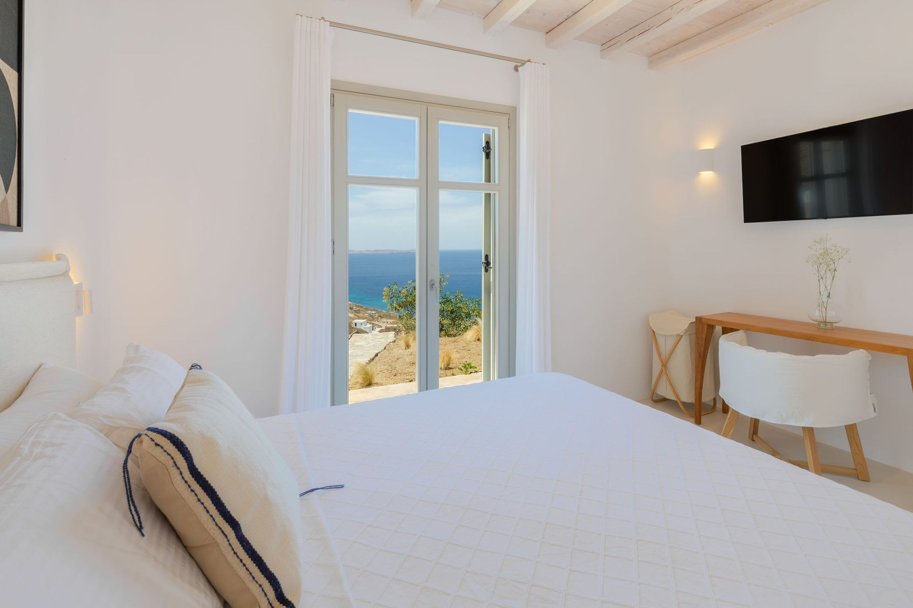 Quarto com uma cama grande, uma escrivaninha e vista para o mar através de uma porta de vidro.
