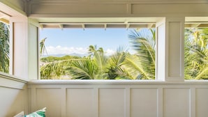 Ein Zimmer mit Blick auf Palmen und Berge, zu sehen durch ein Fenster mit weiß gefasten Wänden.